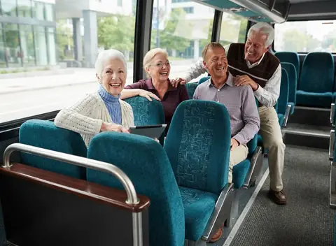 Four smiling senior passengers riding together on a shuttle bus